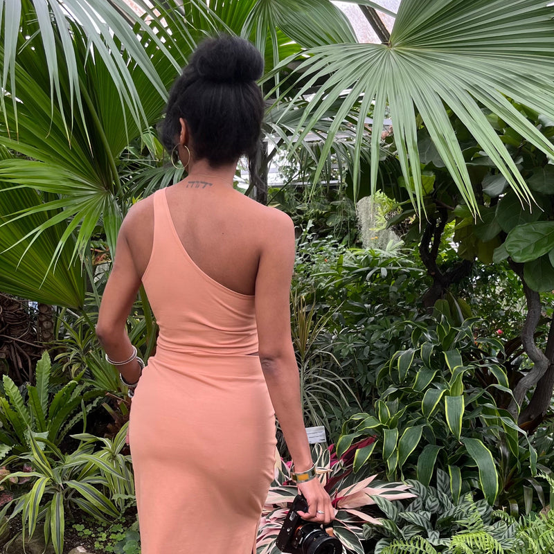 back of woman in tropical plant greenhouse wearing natural fiber asymetrical cropped tank top + skirt in peach colour